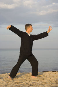 Full length of man practicing tai chi on shore at beach against sky