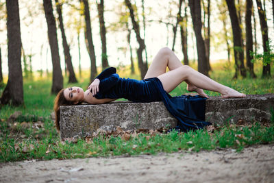 Young woman lying down on land against trees in forest