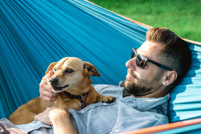 Handsome european man in sunglasses is resting in hammock with his cute little dog.
