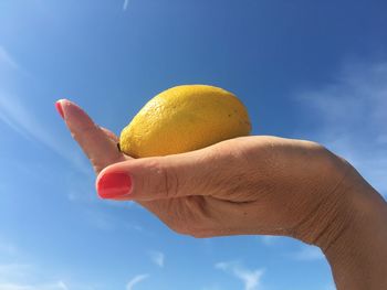 Low angle view of person holding ice cream against blue sky