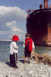 Two fashionable baby boys stand next to a large rio ship that ran aground off novorossiysk