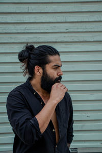 Young man looking away while standing against wall