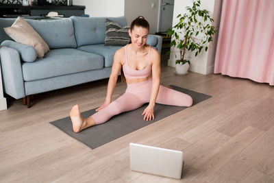 Woman doing yoga online from laptop at home. young female learning the janu sirsasana pose in room. 