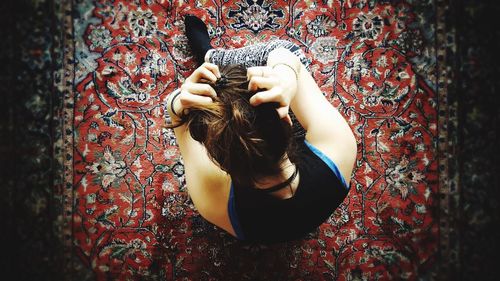 Directly above shot of woman sitting with hands in hair on patterned carpet