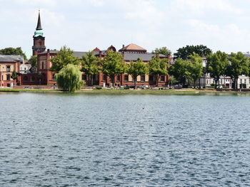 Buildings at waterfront against cloudy sky