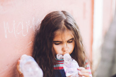 Girl drinking water while leaning on wall