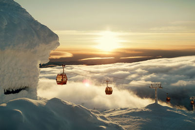 Ski lifts above clouds at sunset