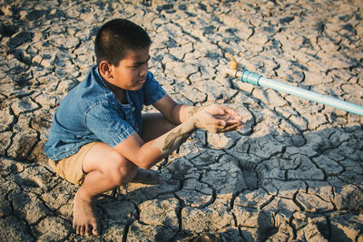 Close-up of boy cupping hands below faucet on cracked field