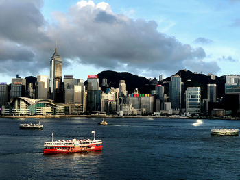 Ferry in victoria harbour by buildings against sky in hong kong