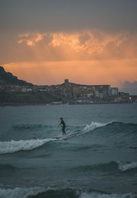 Man surfing on sea against sky during sunset