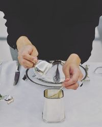 Midsection of person holding spoon in container on table