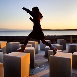 Full length of girl jumping on block shapes at promenade during sunset