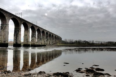 Bridge over river against cloudy sky