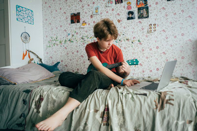 Young woman using laptop while sitting on bed at home