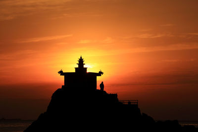 Lighthouse by sea against sky during sunset