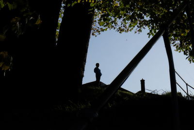 Side view of silhouette man standing by trees against sky