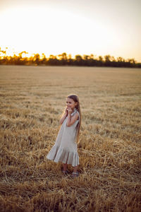 Girl child with long hair walking across the field wearing with long hair during sunset
