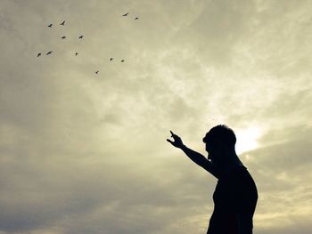 Low angle view of bird flying against cloudy sky