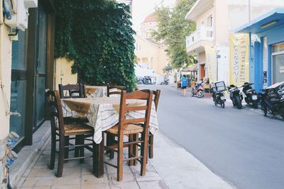 Empty chairs and tables at sidewalk cafe by buildings in city