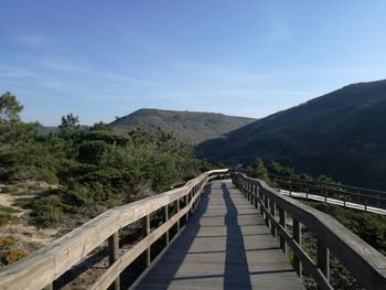 Rear view of man walking on footbridge against sky