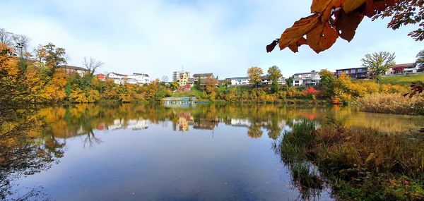 Scenic view of lake by trees and houses against sky