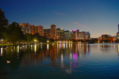Illuminated buildings by lake against blue sky at night