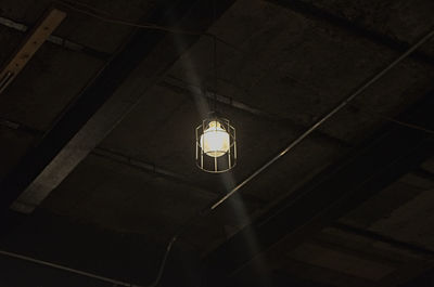 Low angle view of illuminated light bulb hanging on wall in building