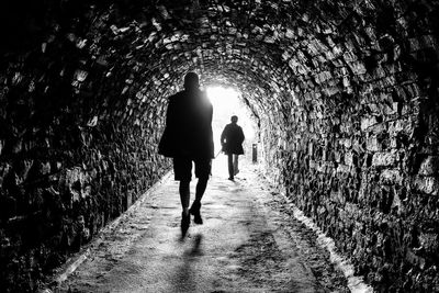 Rear view of people walking on footpath in tunnel