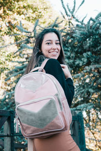 Portrait of smiling young woman standing against trees