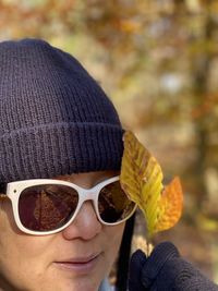 Close-up of woman wearing sunglasses holding autumn leaves