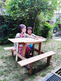 Siblings playing while sitting on bench in park