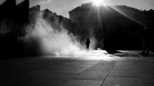 Silhouette person walking by smoke on footpath during sunny day