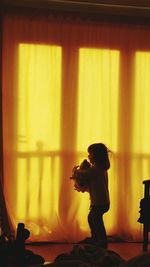 Side view of girl with toy standing on floor at home