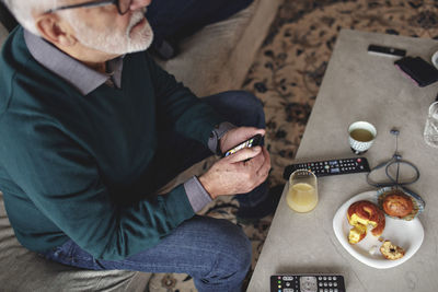 High angle view of senior man with smart phone while sitting on sofa in living room