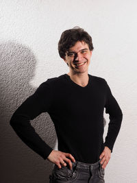 Portrait of smiling man with hands on hip standing against white wall