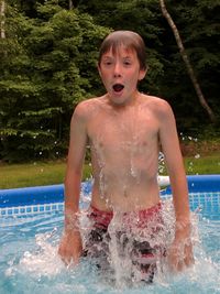 Portrait of shirtless boy enjoying in wading pool at yard