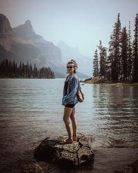 Full length of man standing on rock by lake against sky