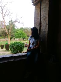 Woman sitting on plant against building