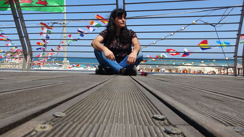 Woman sitting on wood against sky