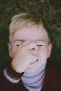 Close-up of playful boy holding nose while lying on field