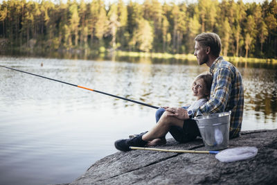 Portrait of smiling daughter fishing with father while sitting by lake