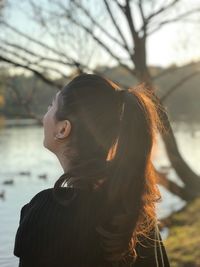 Rear view of young woman standing at lakeshore during sunset