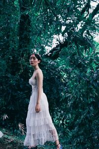 Portrait of young woman standing against tree in forest