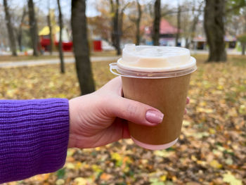 Hand holding coffee cup in autumn park with leaves on background