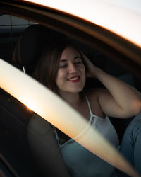 Portrait of a smiling young woman in car at sunset