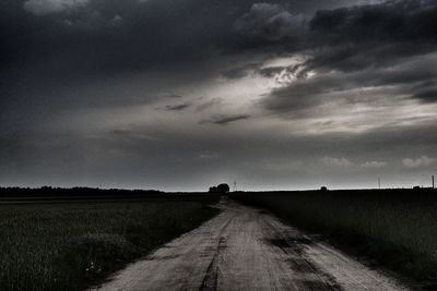 Dirt road amidst field against sky
