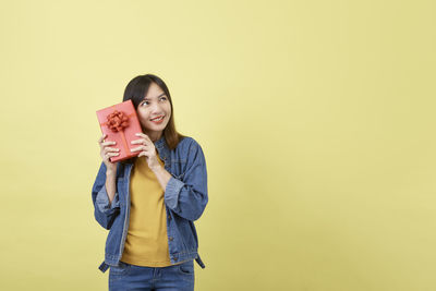 Portrait of smiling young woman against yellow background