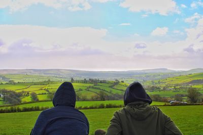 Rear view of people looking at field against sky