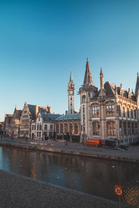 Buildings by river against clear blue sky