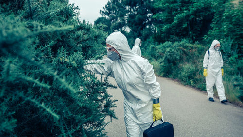 People wearing protective suit standing by trees on road
